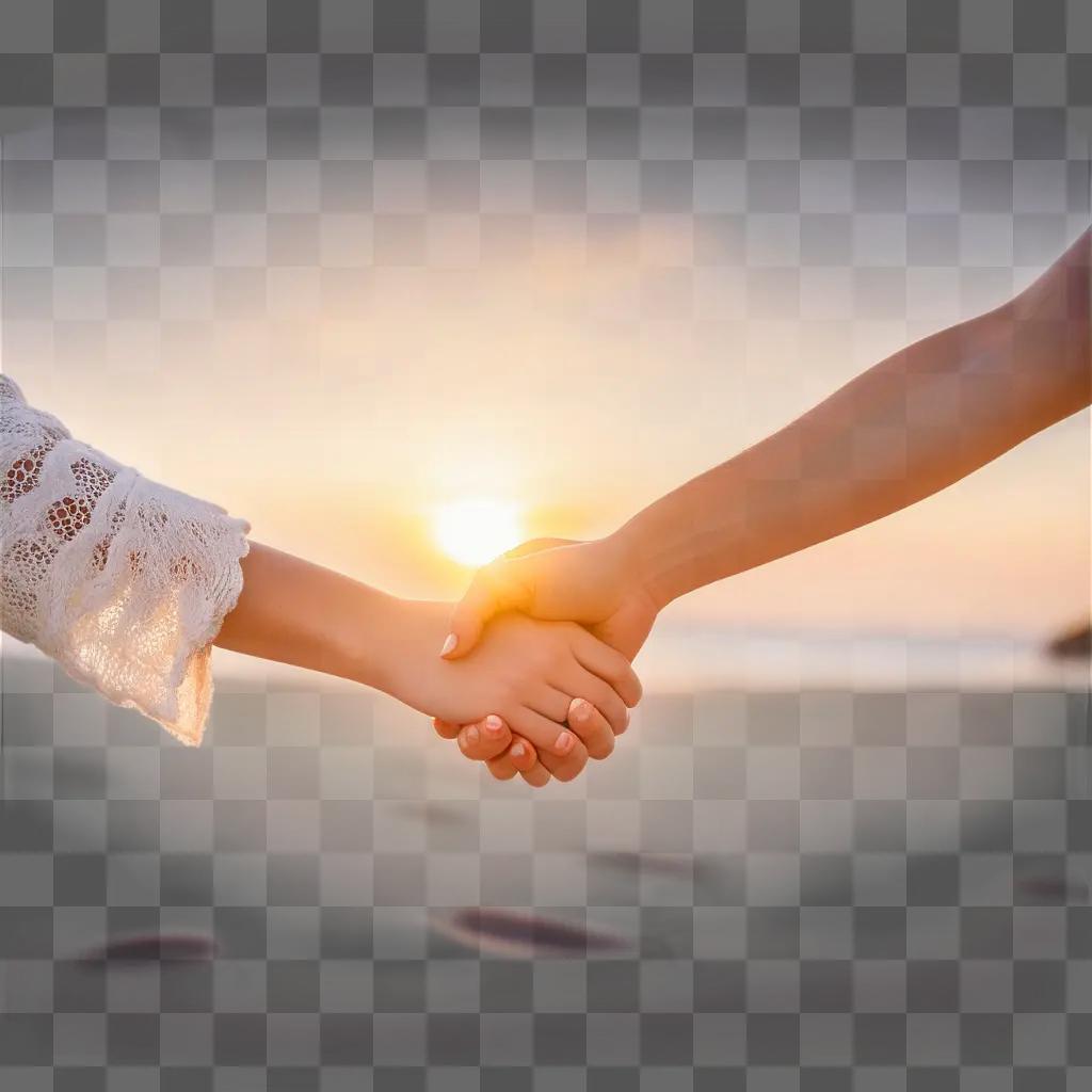 Two hands holding each other on a beach at sunset